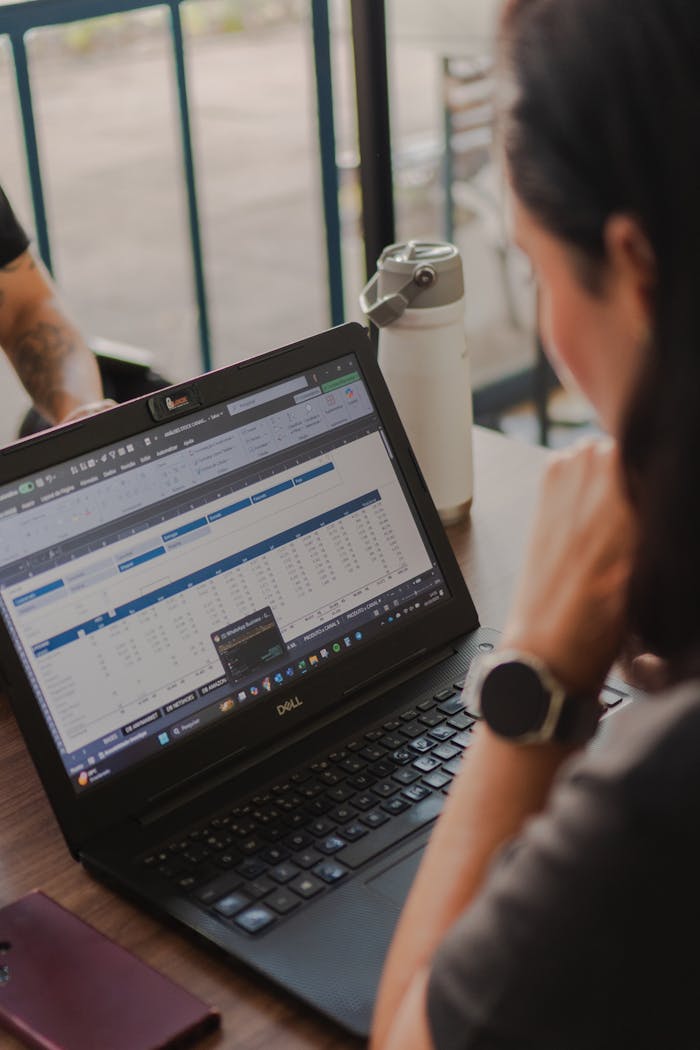 Close-up of a person reviewing a spreadsheet on a laptop in a cafe setting.