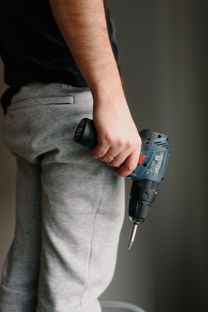 Crop anonymous male in casual clothes holding drill while renovating interior of apartment